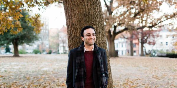 Ali Wyne leanign on a tree on a north eastern university looking campus in the fall 