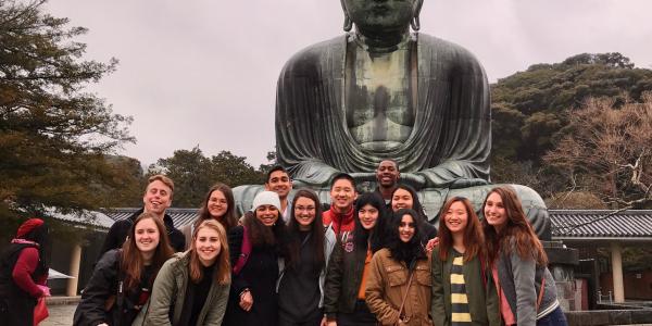 students smile in front of large buddha statue